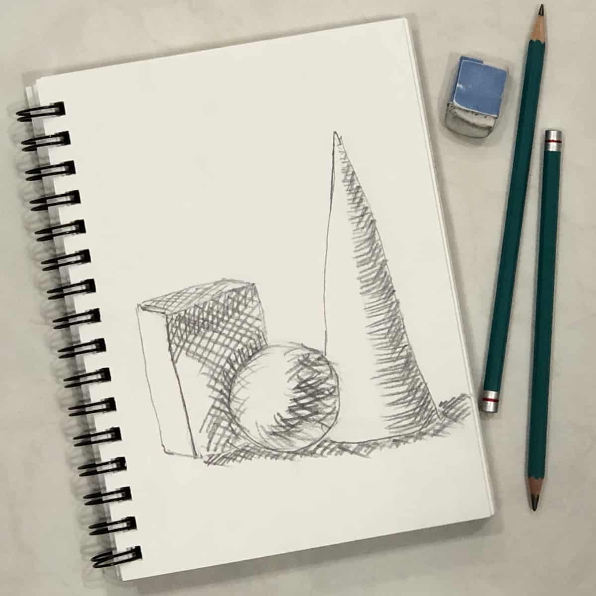 Cross hatched drawing of a cone, sphere, and box on a spiral ring sketchbook next to some drawing pencils and an eraser.