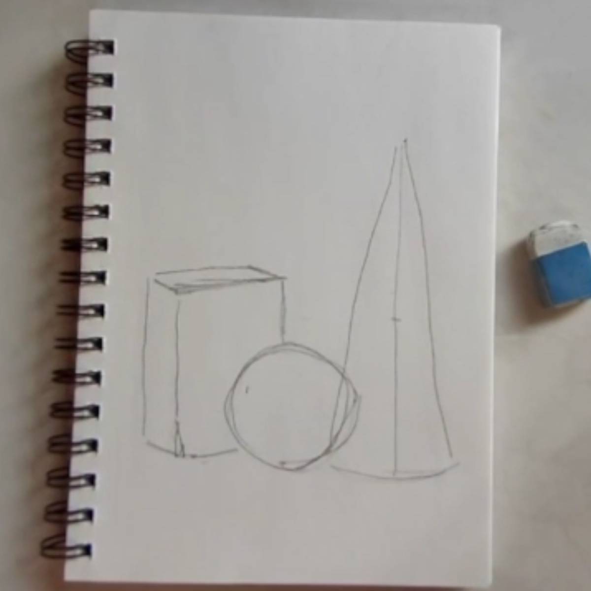 Sketch of a cone, sphere, and box on a spiral ring notebook with an eraser. 