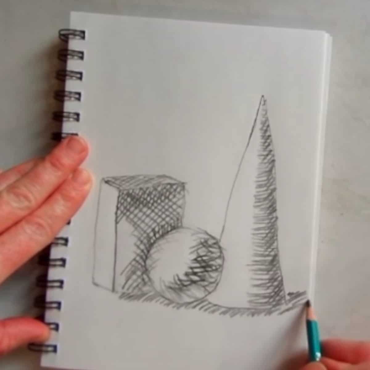 Artist adding cross hatching lines for shading on a sketch of a cone, sphere, and box on a spiral ring notebook. 