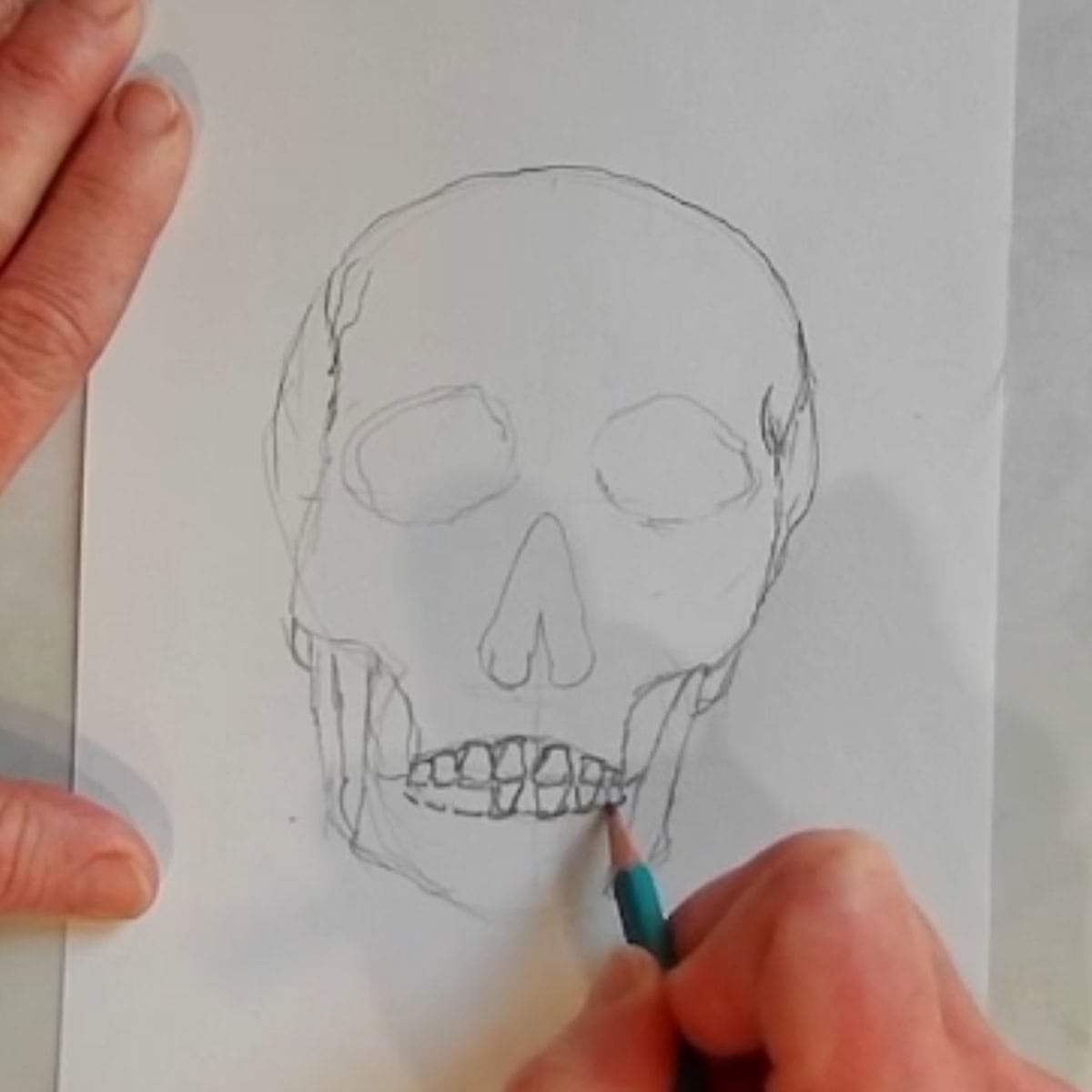 Beginning sketch of a skull with artist drawing in the teeth with a pencil. 