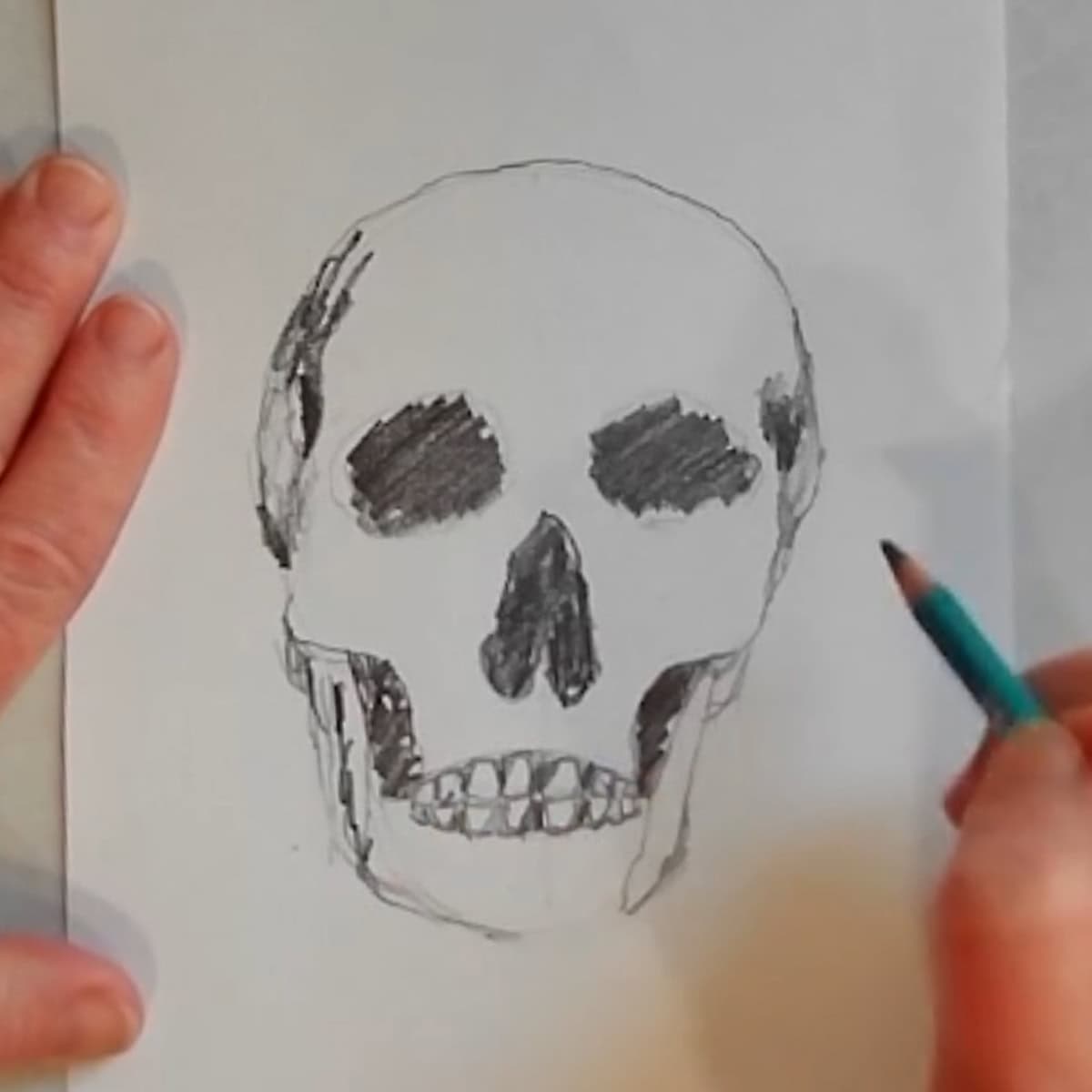 Beginning drawing of a skull with artist shading in dark areas with a pencil. 