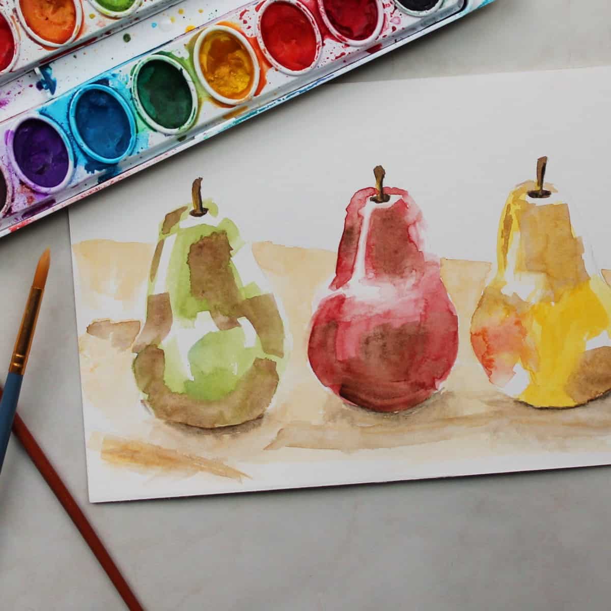 Watercolor painting of pears next to brushes and watercolor paint set.