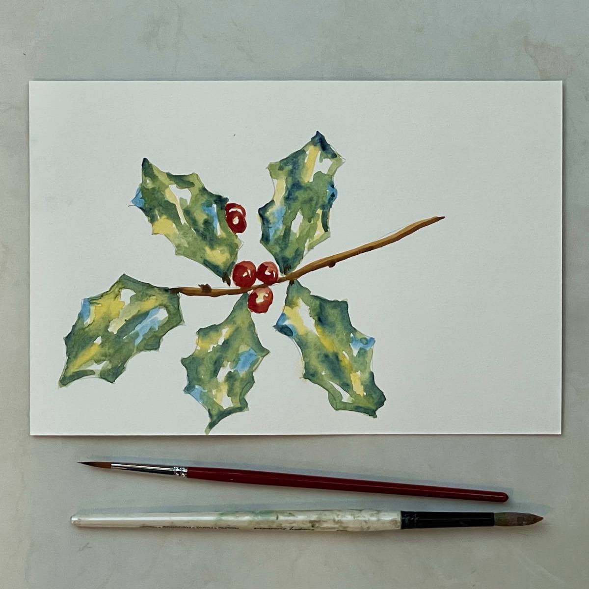 Watercolor painting of a spring of holly with paint brushes.