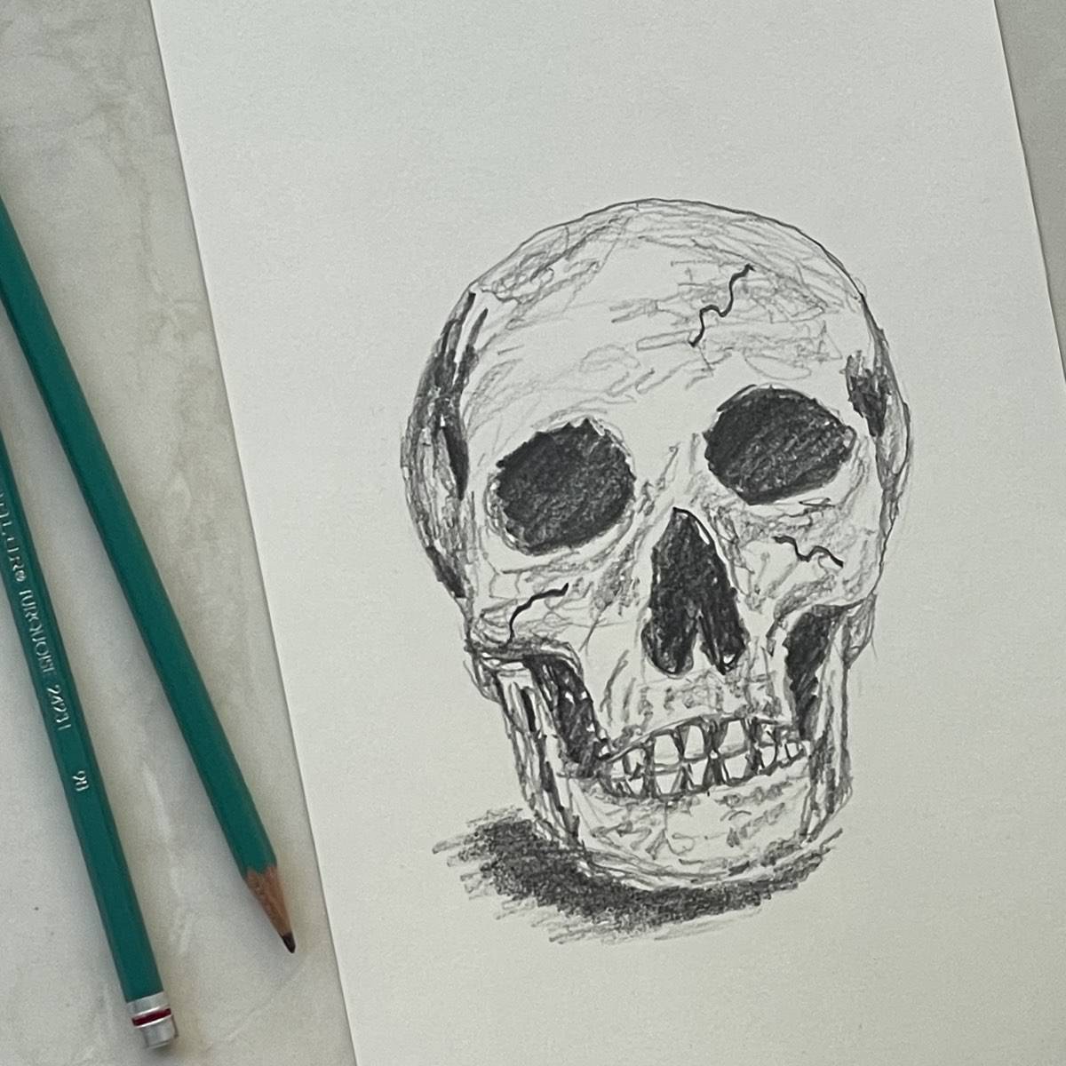 Drawing of a skull in pencil next to artist drawing pencils and an eraser.