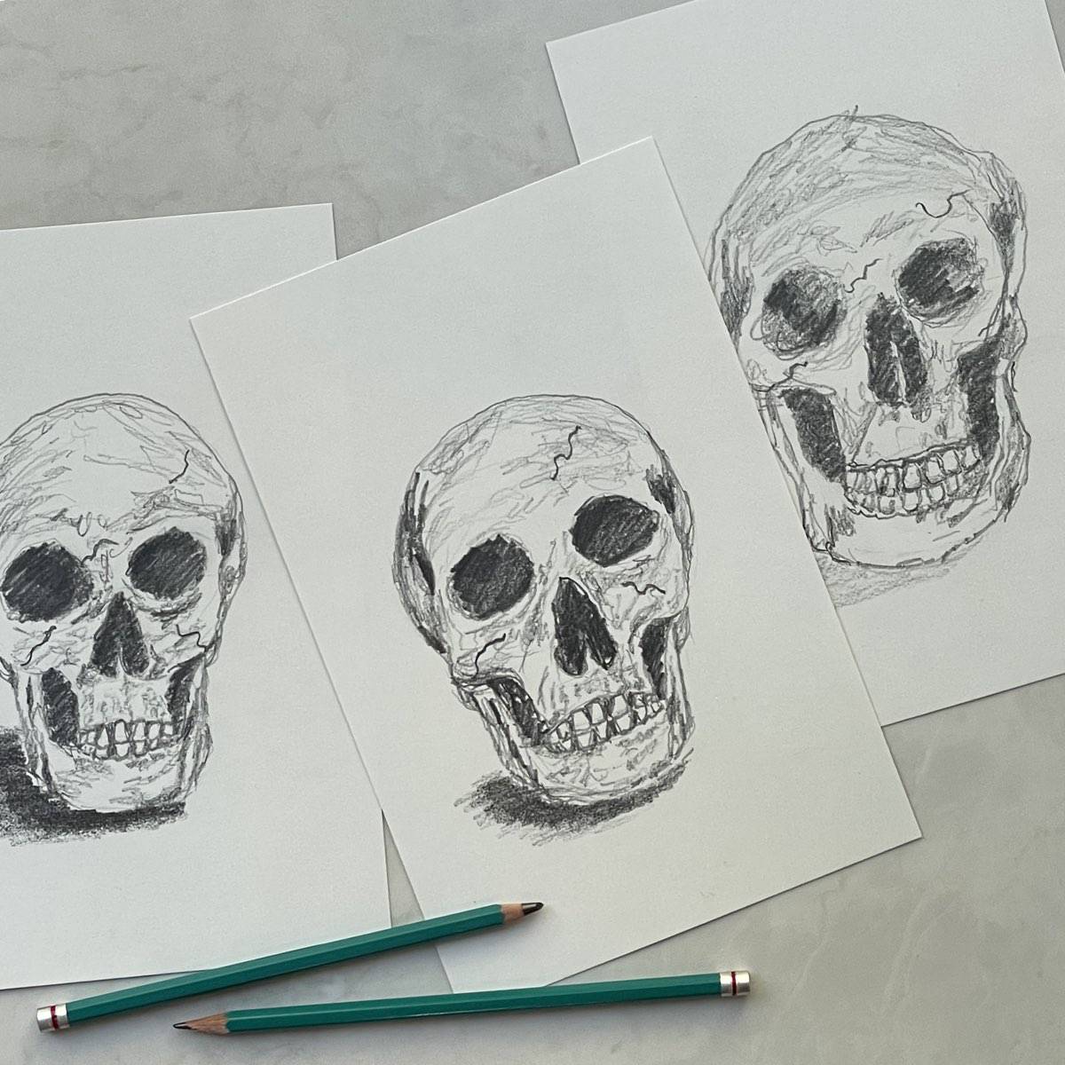 Three sketchy drawings of skulls next to artist drawing pencils.