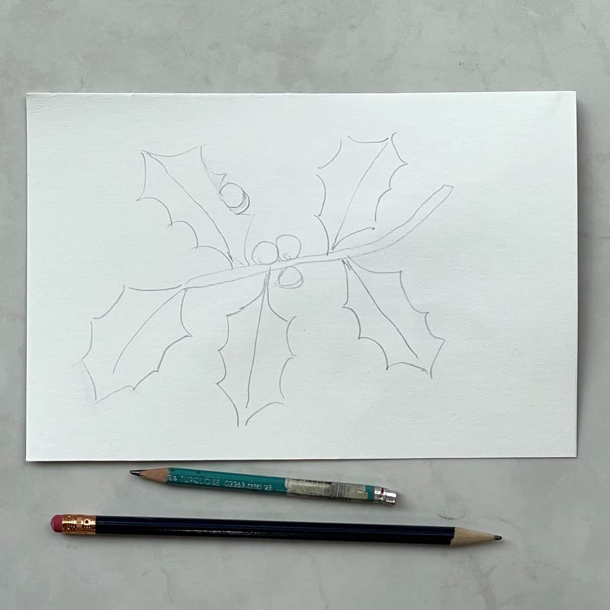 A light pencil sketch of holly leaves next to some drawing pencils.