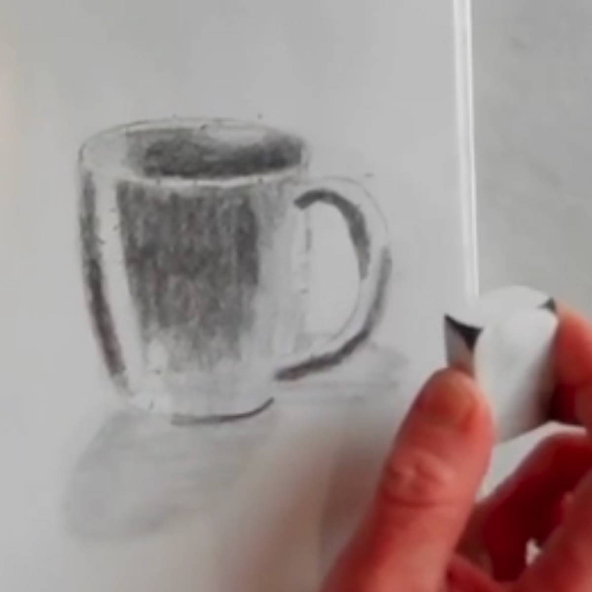 Erasing some highlighted areas on a pencil drawing of a coffee mug.