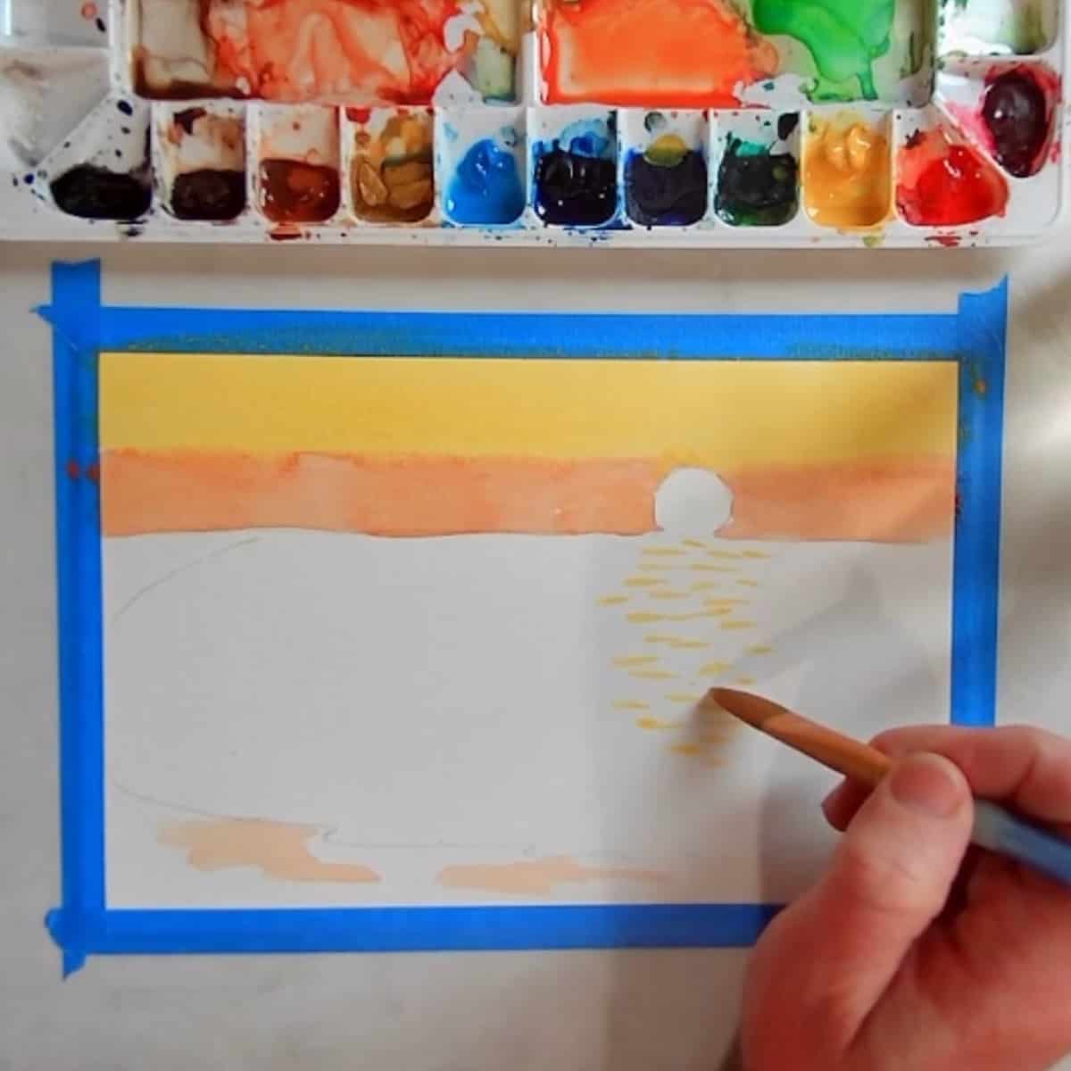 Artist painting in a reflective beach sunset in watercolors.