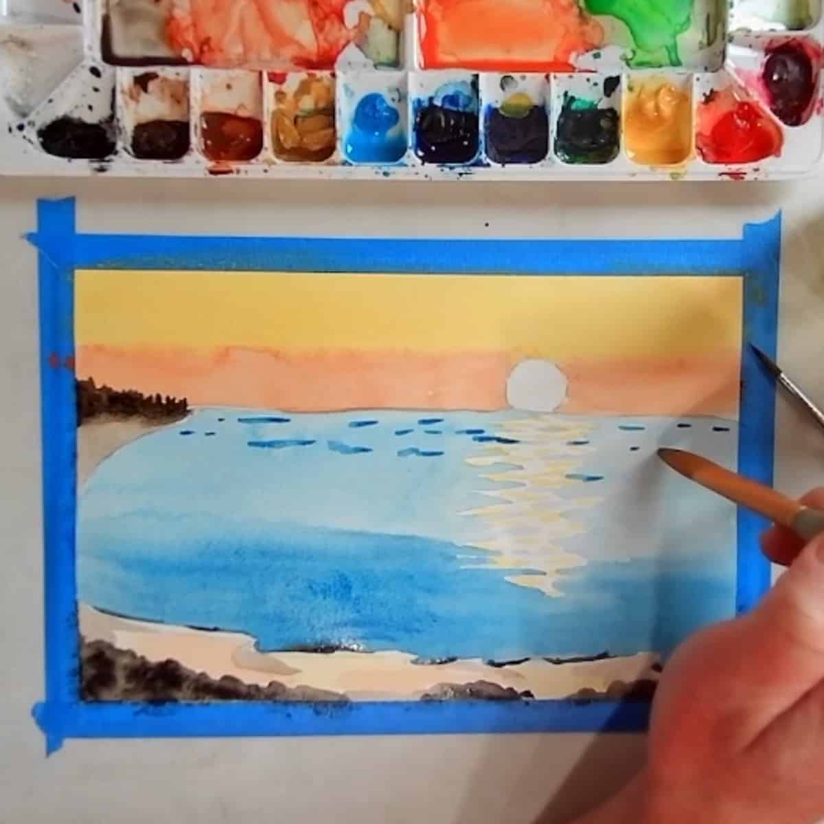 An artist adds in details in the waves and water of a watercolor beach sunset.