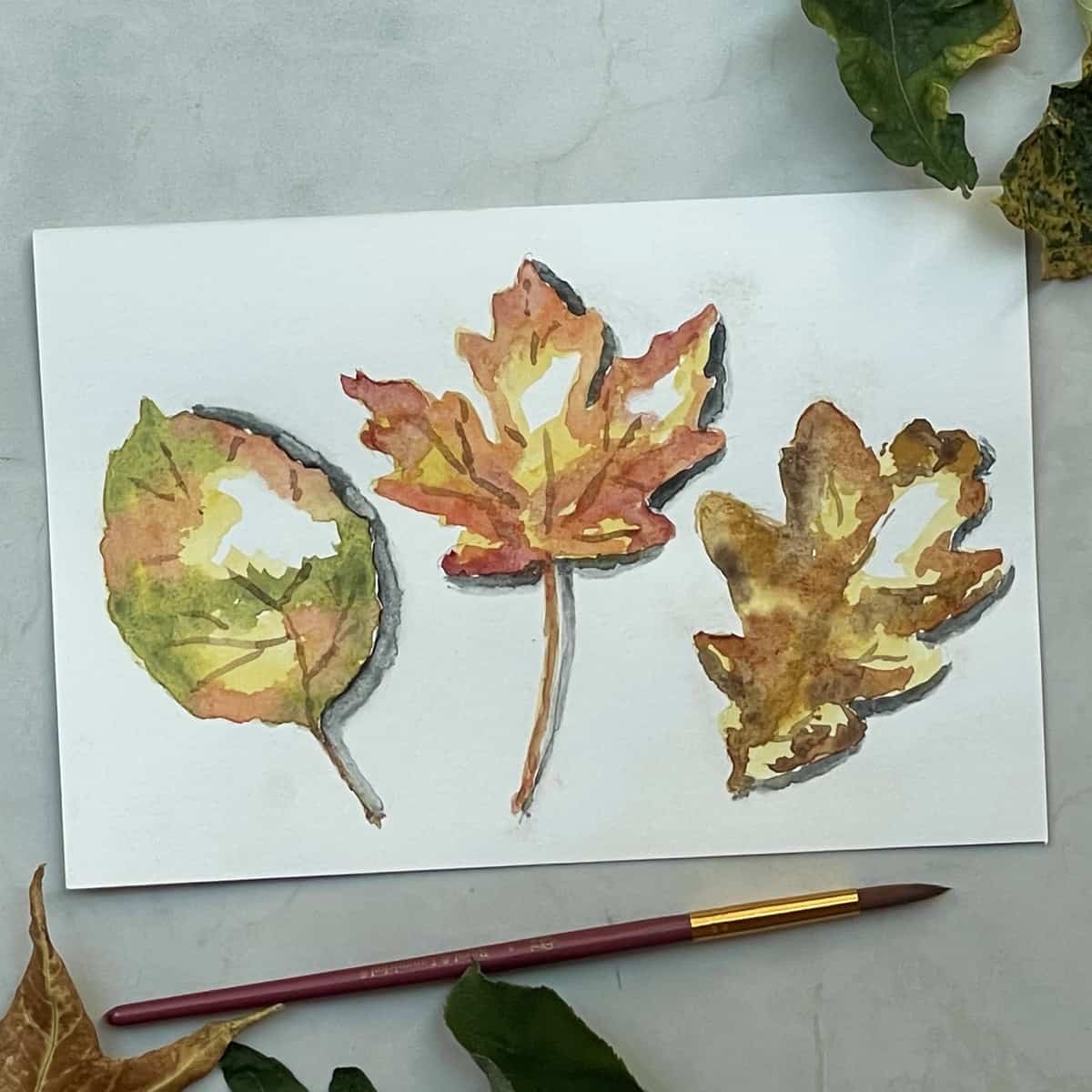 A watercolor painting of three colorful fall leaves next to a paintbrush and leaves.