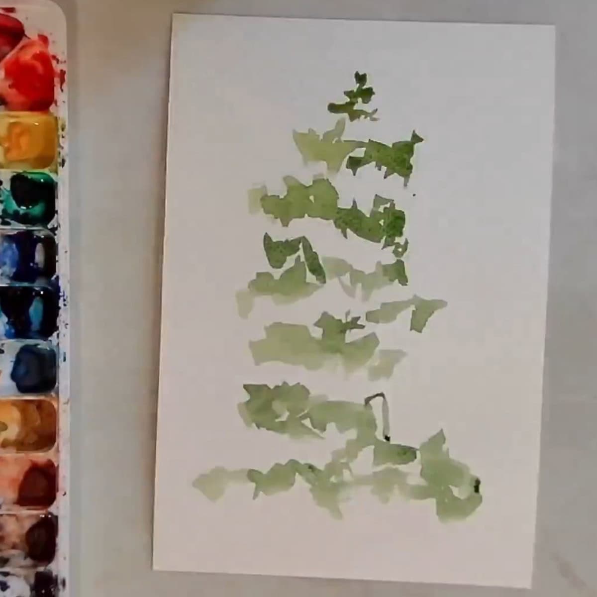 Beginning painting of a watercolor pine tree next to a paint palette.