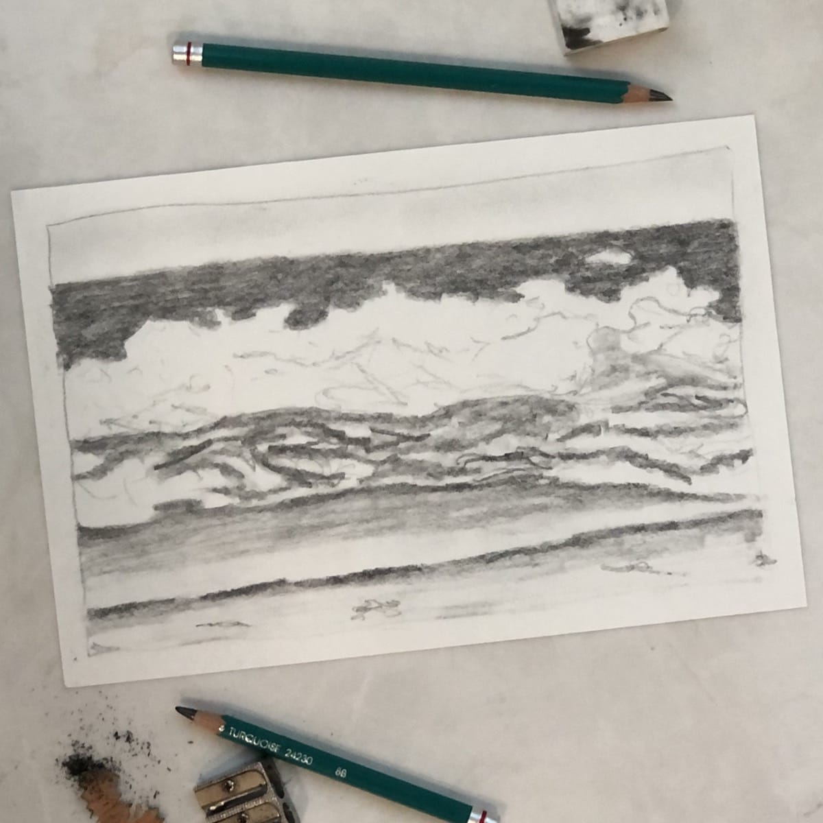 A pencil drawing of a seascape with drawing pencils, a pencil sharpener, and an eraser.
