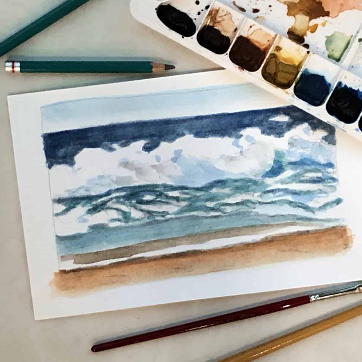 Watercolor painting of a seascape with watercolor paints, paintbrushes, and drawing pencils.