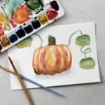 Watercolor painting of a pumpkin with watercolor paint and brushes.