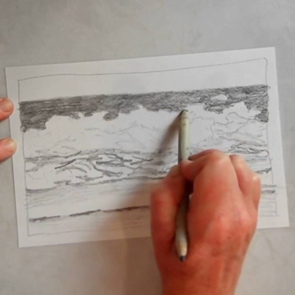 A hand using a blending stump to blend pencil shading in an oceans cape.