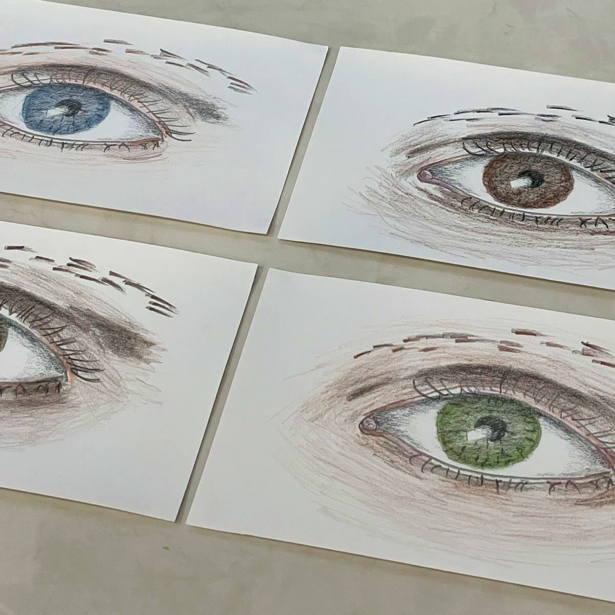 Colored pencil sketches of eyes up close on drawing paper.