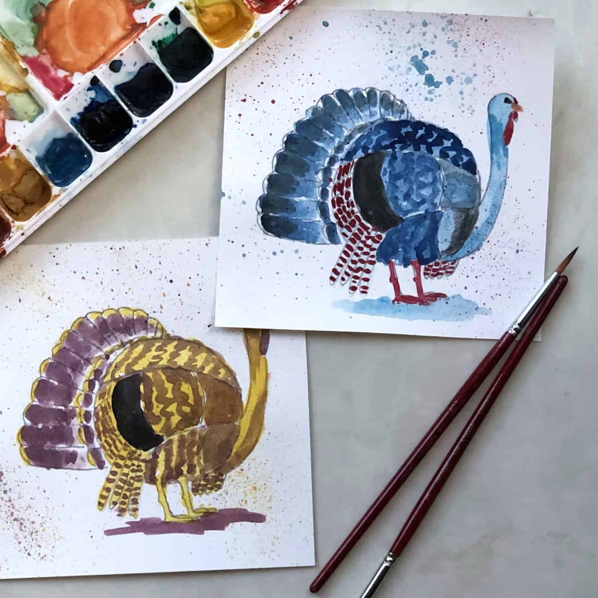 Two watercolor paintings of turkeys in bright colors with splatters next to a watercolor paint set and some paint brushes.