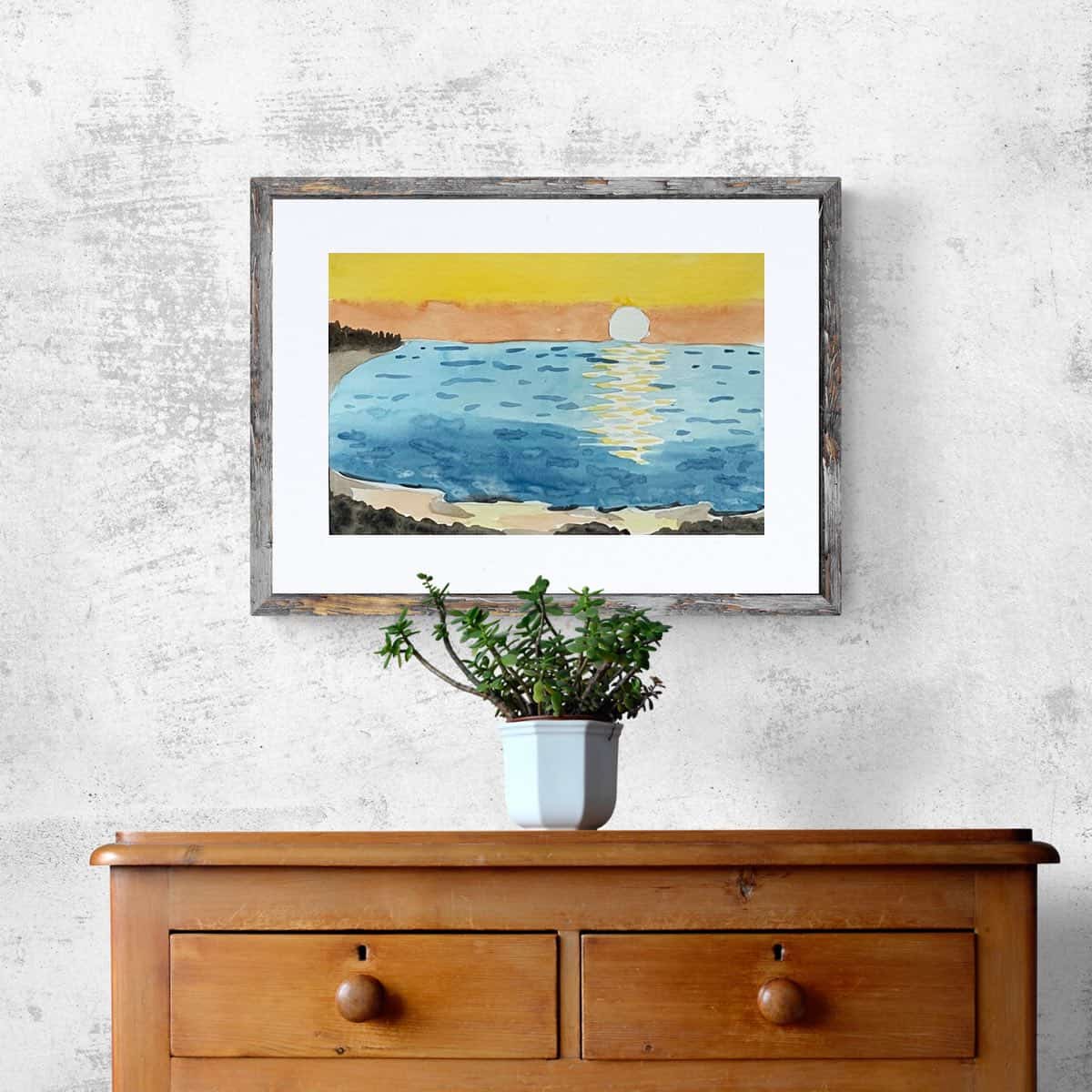 A watercolor painting of a beach sunset hanging on a wall above a cabinet with a plant.