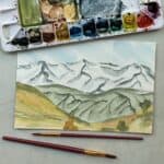 Painting of a mountain landscape with watercolor paint and paintbrushes.