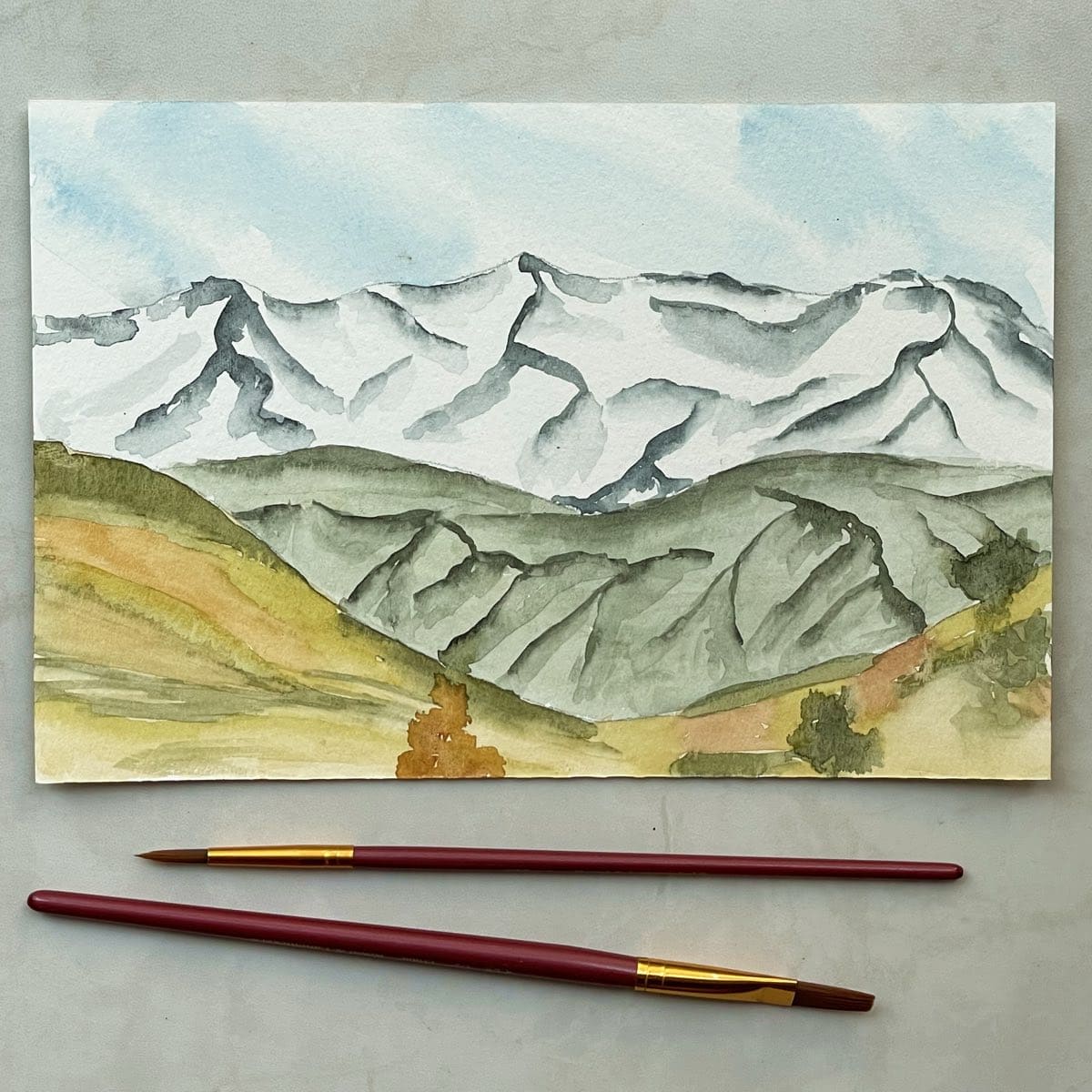 Painting of a mountain landscape with paintbrushes.