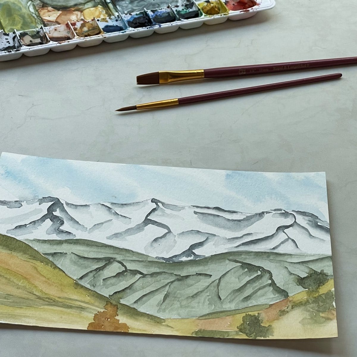 Painting of mountain scenery with watercolor paint and brushes.