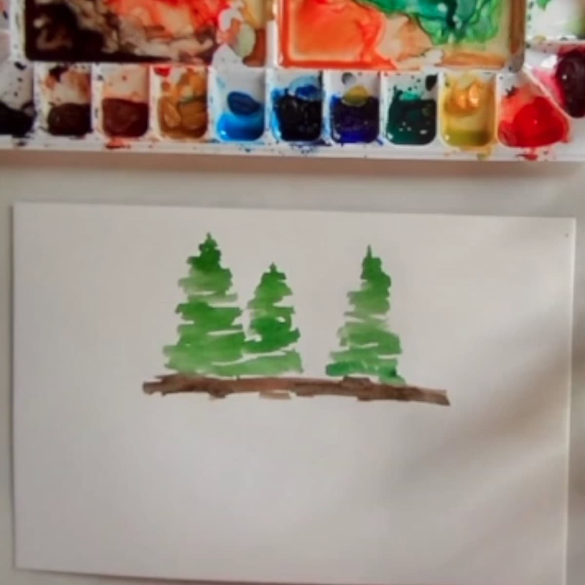 The beginning of a watercolor painting of trees on land.