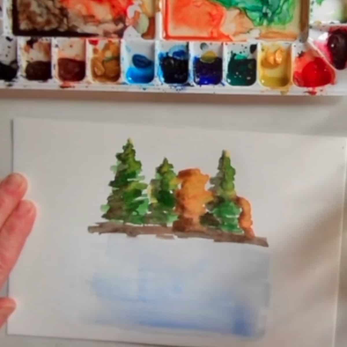 Blue is added below the trees in the watercolor painting for the water.
