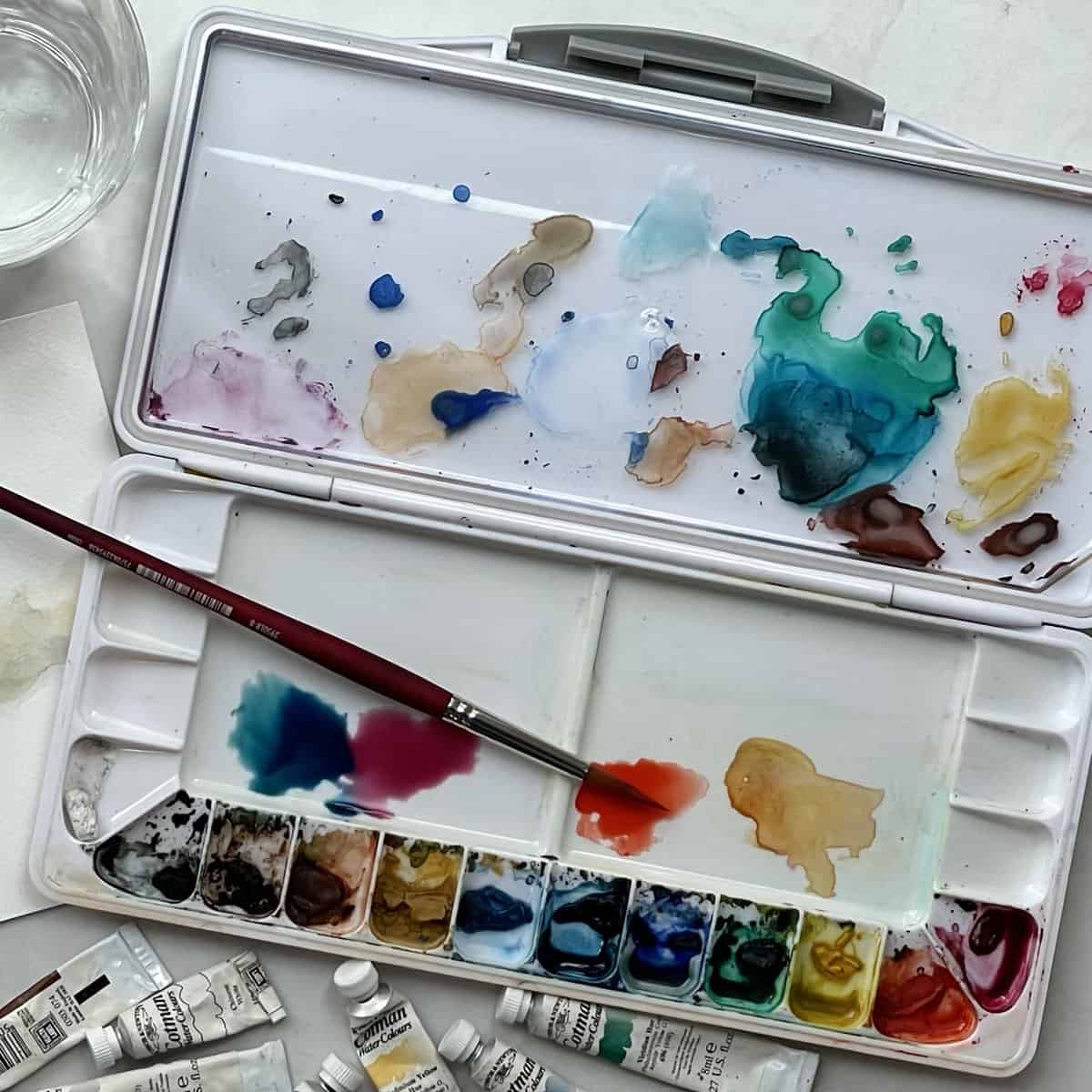 A watercolor palette box with paint and a paintbrush.