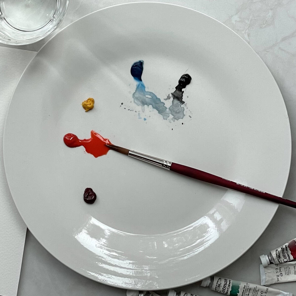 A white dinner plate being used as a watercolor palette with paint and a paintbrush.